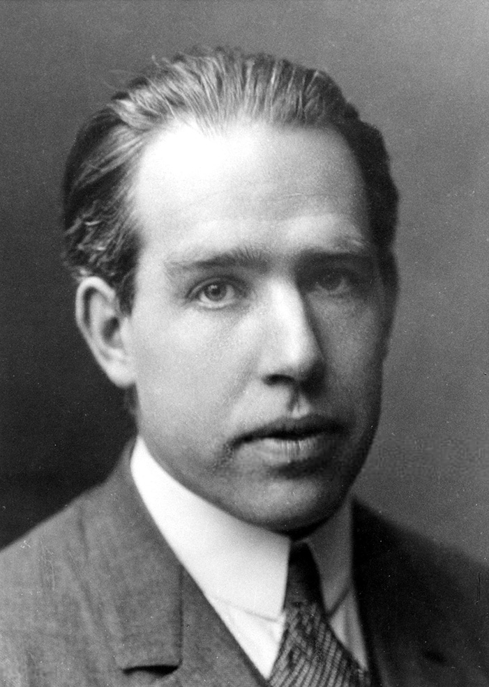 Bohr in a suit looking at the camera. His hair is slicked back.