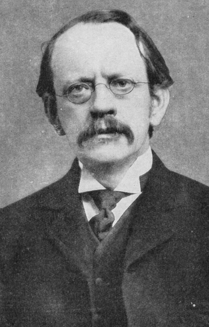 JJ Thomson in a suit and tie looking at the camera.
